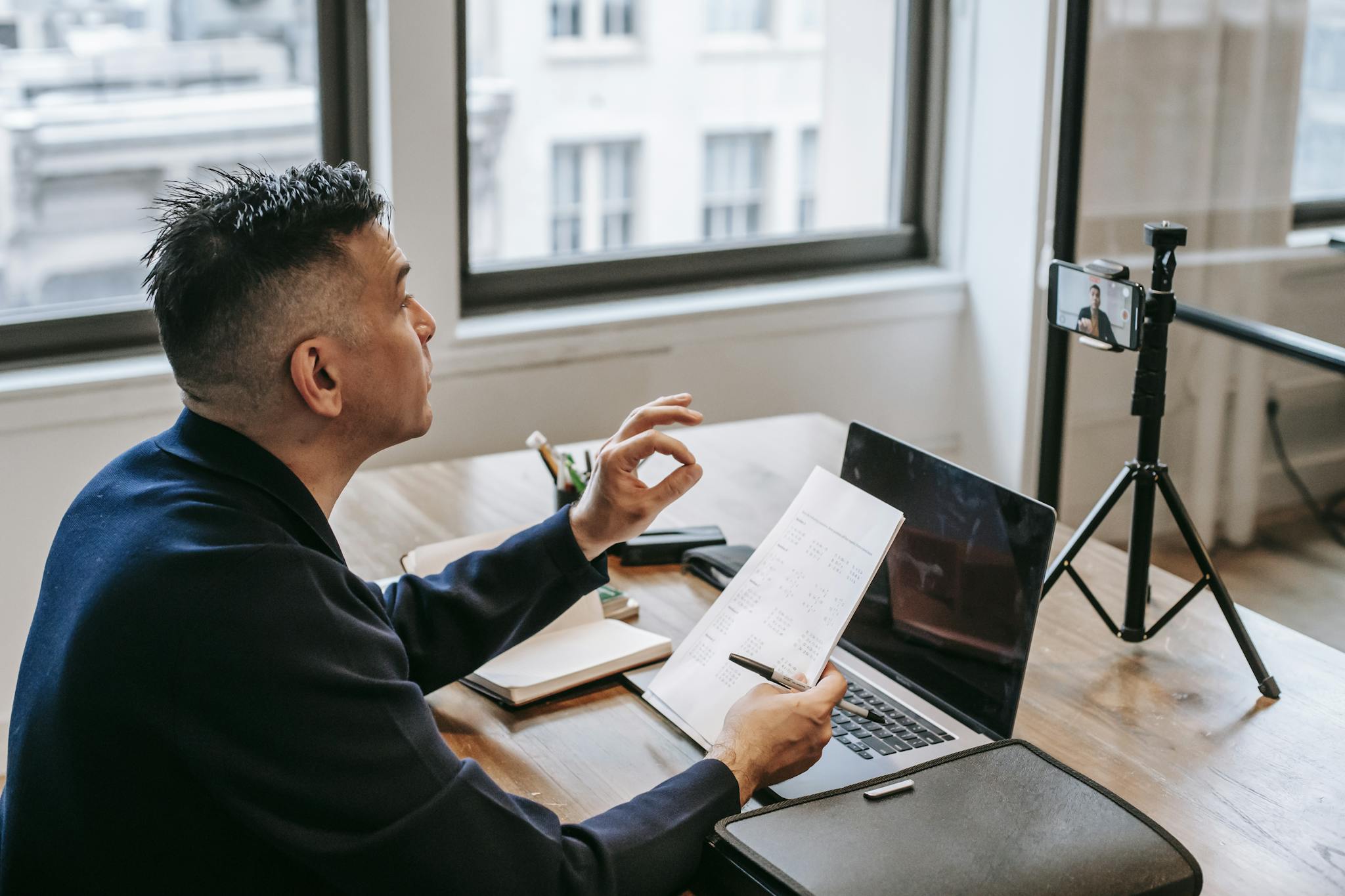 Home 11 Man using laptop and smartphone for a video call in an office setting.